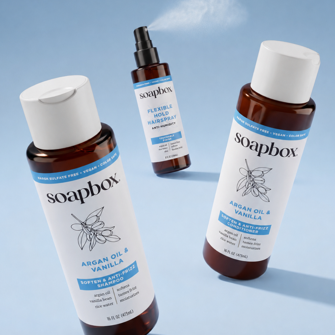 Soapbox anti-humidity flexible hold hairspray with spray nozzle shown between argan oil shampoo and conditioner bottles on bl