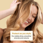Woman with long, wavy honey-blonde hair running hand through strands against beige background.