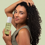 Person holding Soapbox Jasmine Pistachio hair fragrance mist bottle with white cap against pale green background.