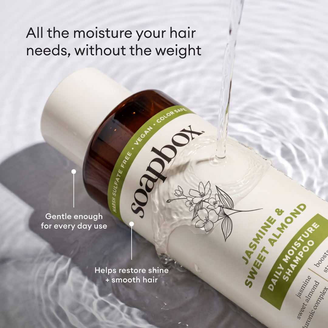 Cream-colored shampoo bottle with brown cap and green label featuring jasmine flower illustration, positioned on white fabric