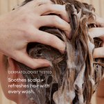 Hands massaging lathered shampoo into brown hair during shampooing.