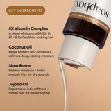 Dark bottle with white label and tan band listing key ingredients: vitamin complex, coconut oil, shea butter, and jojoba oil 