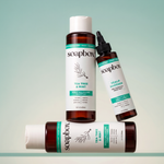 Three soapbox hair care bottles with white caps and amber-colored liquid against a pale green background.