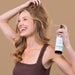 Woman holding Soapb Flexible Hold Hairspray bottle with wavy brown hair against tan background.