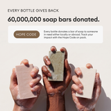 Three hands holding bars of soap in pink, tan, and white colors with visible texture.