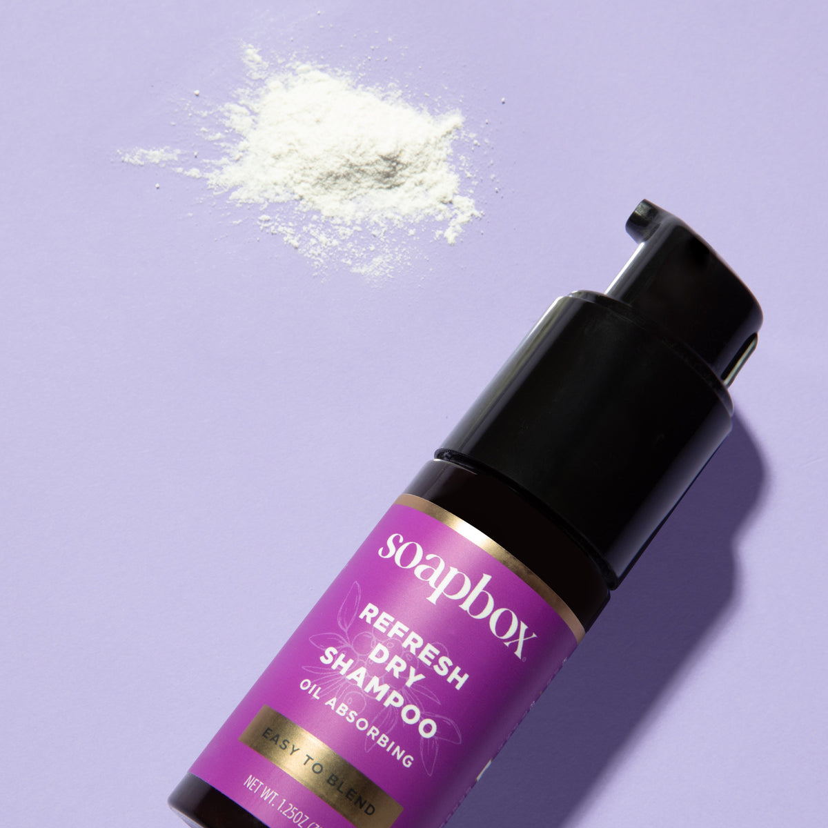 Black aerosol bottle with magenta label reading "soapbox Refresh Dry Shampoo Oil Absorbing" displayed with loose powder on pu