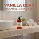 Amber bottle of Soapbox Vanilla Bean hand soap with pump dispenser on bathroom counter next to white bowl, towels, and plant.