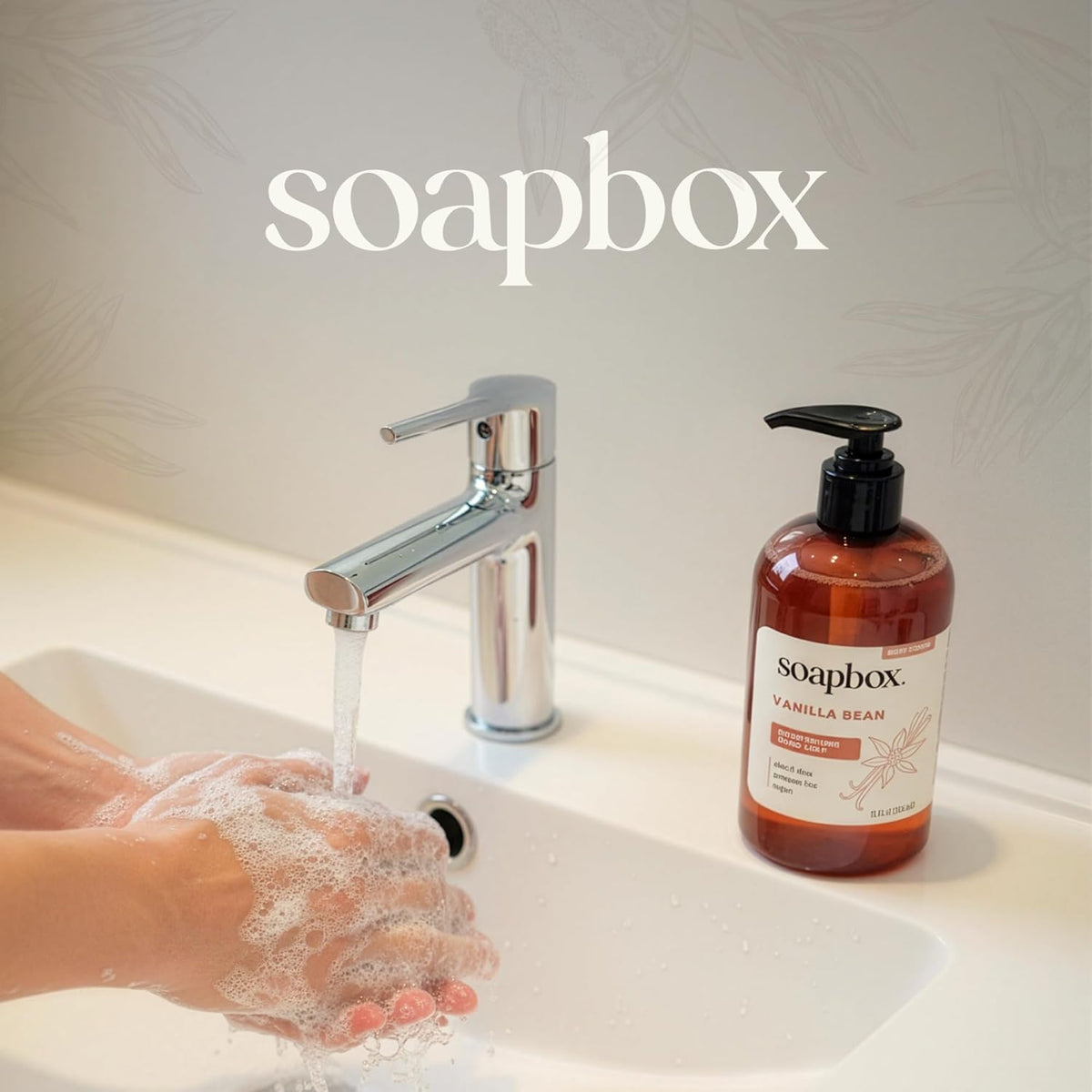 Soapbox Vanilla Bean liquid hand soap in amber bottle with black pump dispenser next to chrome faucet and soapy hands.