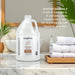 White gallon bottle of Soapbox liquid hand soap with white cap, displayed next to folded white towels on marble countertop.
