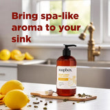 Amber glass pump bottle of Soapbox Meyer Lemon + Tea Leaves hand soap displayed on wooden board with fresh lemons and dried t