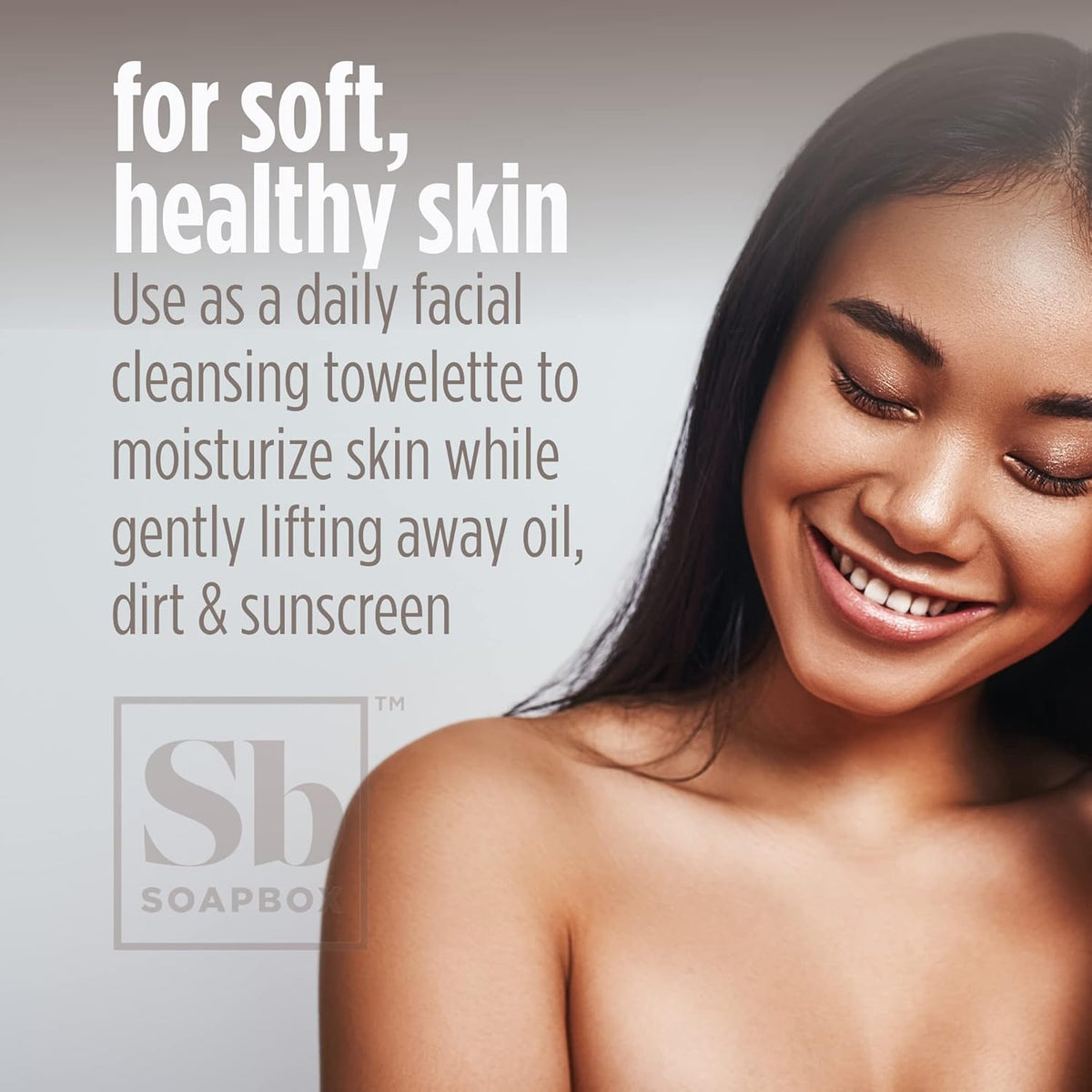 Woman with closed eyes smiling while holding a white makeup remover wipe packet against her shoulder.