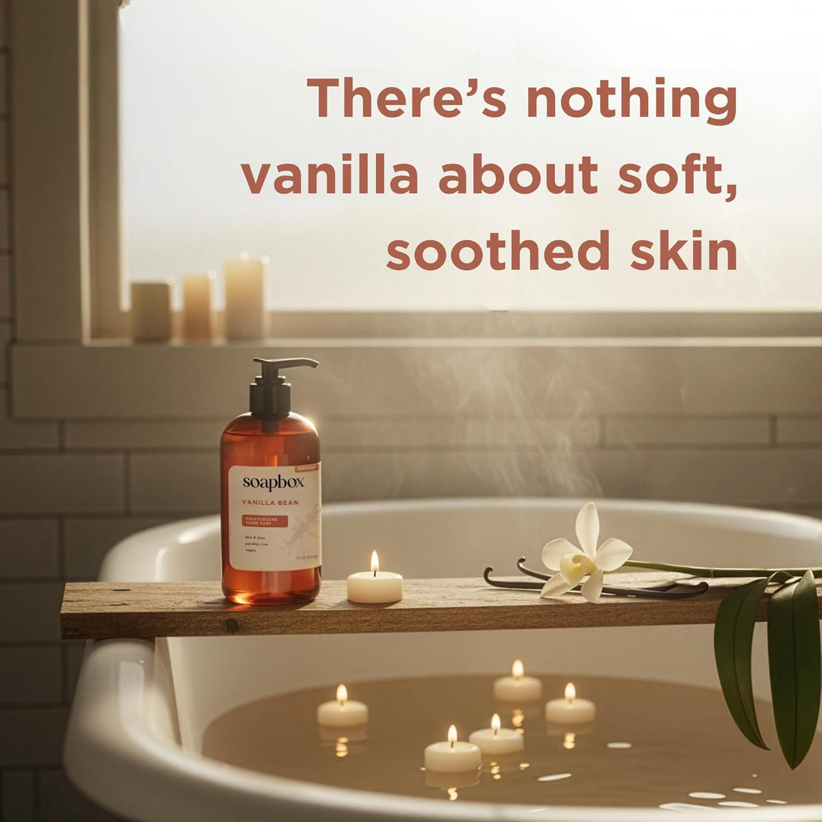 Amber liquid hand soap bottle with black pump dispenser on wooden tub ledge beside candles and vanilla flower.