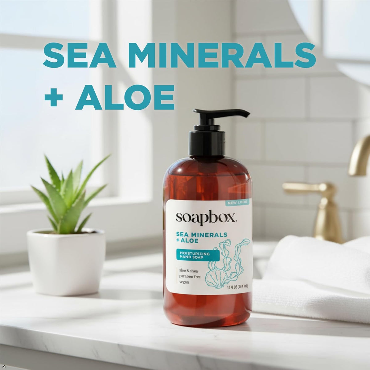 Soapbox liquid hand soap bottle with pump dispenser on bathroom counter next to potted plant and towel.