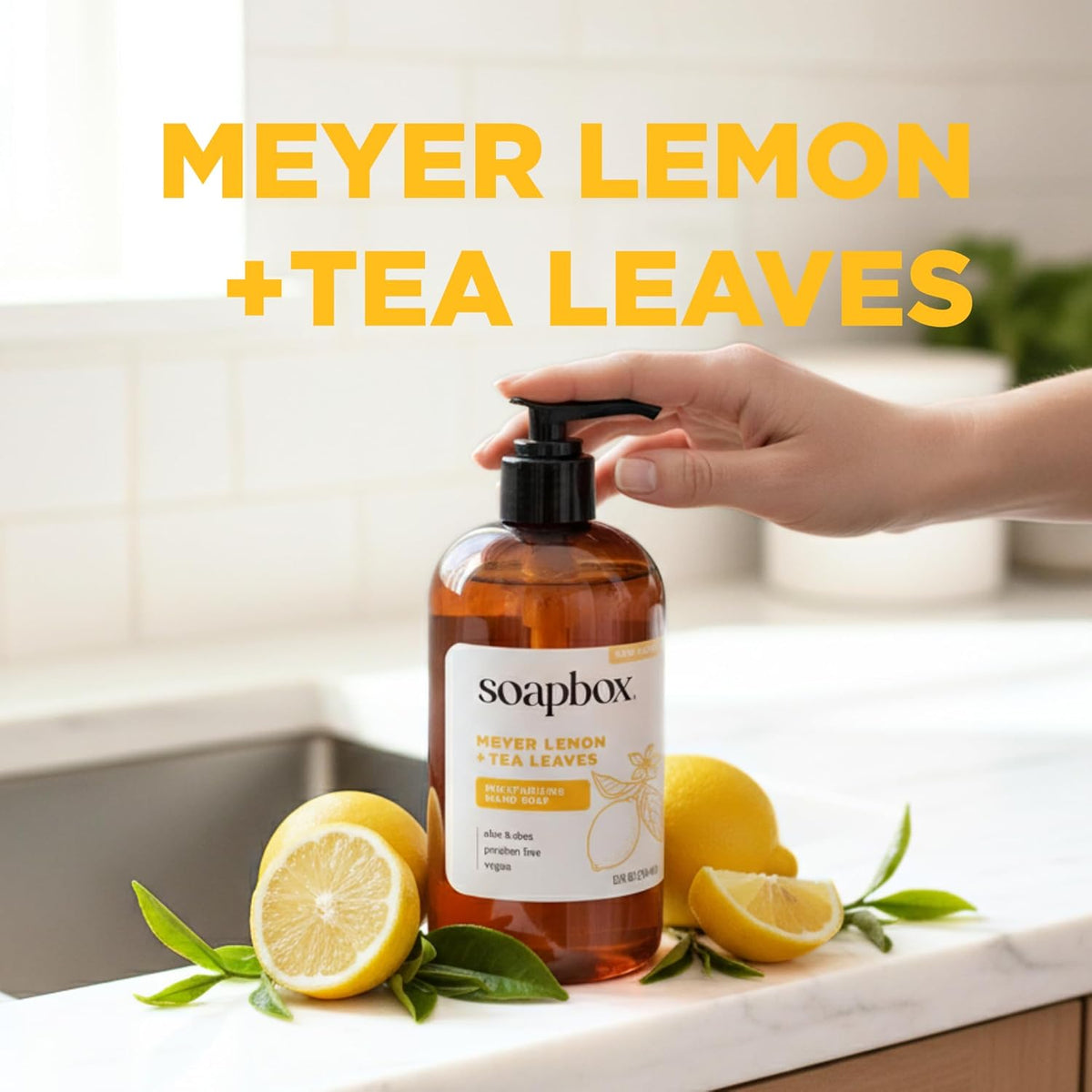 Amber glass bottle of Soapbox hand soap with black pump dispenser, surrounded by sliced meyer lemons and green tea leaves on 