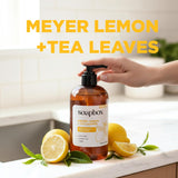 Amber glass bottle of Soapbox hand soap with black pump dispenser, surrounded by sliced meyer lemons and green tea leaves on 