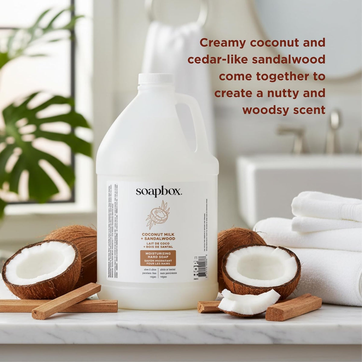 Soapbox gallon refill bottle surrounded by halved coconuts, cinnamon sticks, and folded white towels on marble surface.