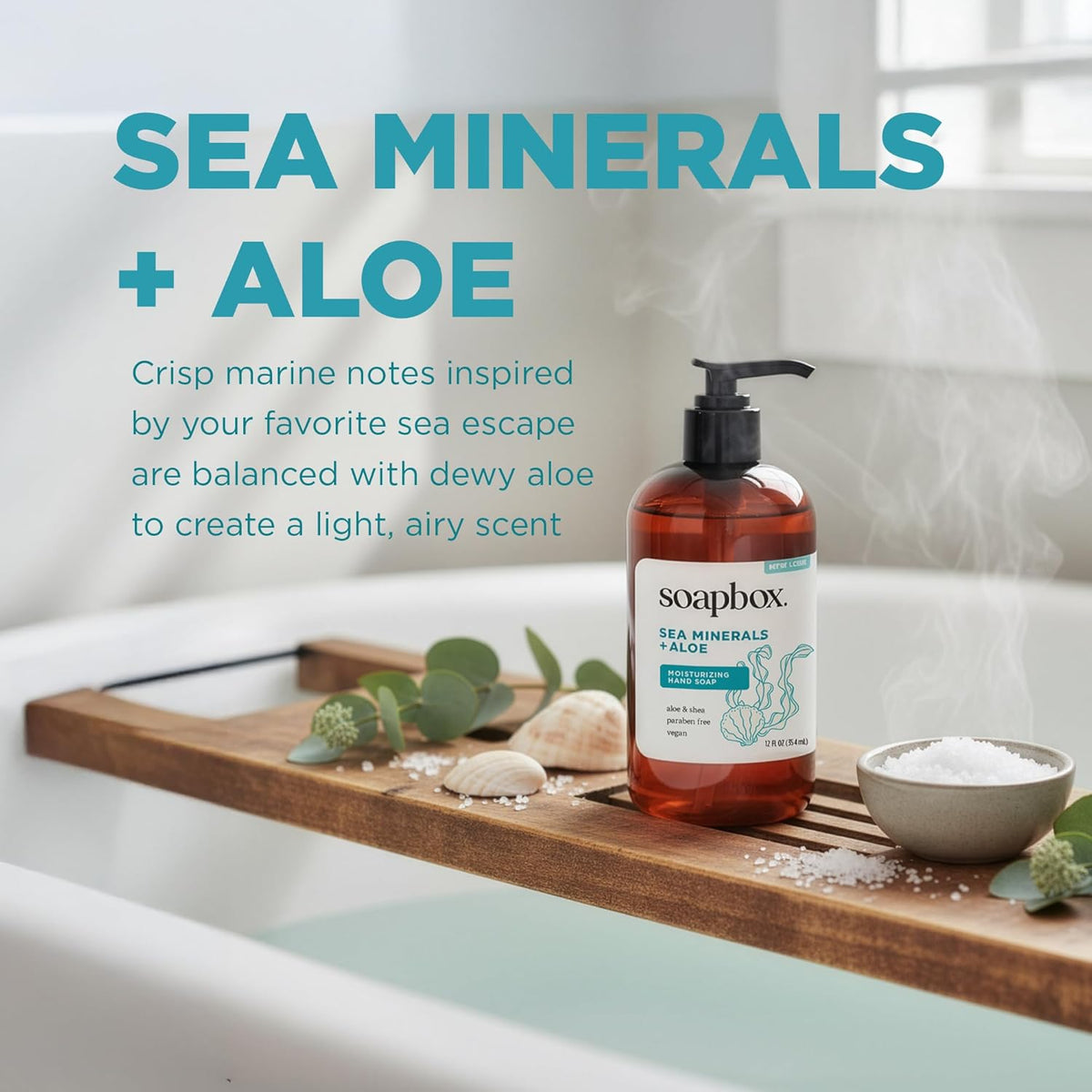 Amber-colored liquid hand soap bottle with black pump dispenser on wooden tray with sea salt and greenery.