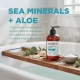 Amber-colored liquid hand soap bottle with black pump dispenser on wooden tray with sea salt and greenery.
