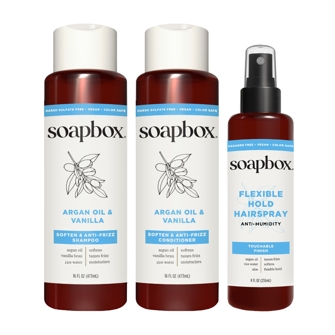 Three Soapbox hair care products: two dark amber bottles with white labels containing Argan Oil & Vanilla shampoo and conditi
