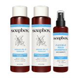 Three Soapbox hair care products: two dark amber bottles with white labels containing Argan Oil & Vanilla shampoo and conditi