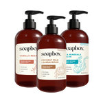 Three dark amber pump bottles of Soapbox liquid hand soap with labels for Vanilla Bean, Coconut Milk + Sandalwood, and Sea Mi
