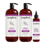 Three dark red Soapbox haircare bottles: two large pump bottles labeled "Biotin & Superfruit Restore & Volume Shampoo" and "C