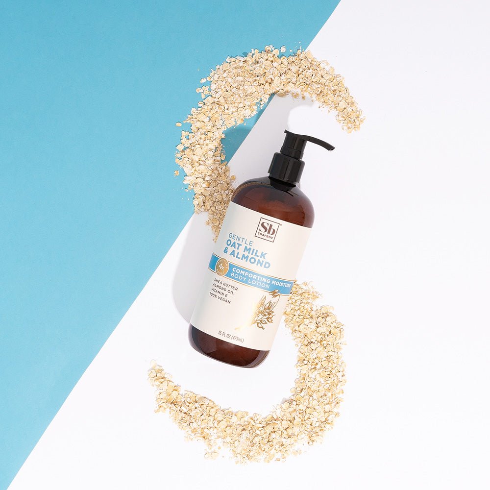 Amber glass pump bottle of oat milk and almond body lotion surrounded by scattered oats on blue and white background.