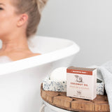 Coconut oil shampoo bar in cream and speckled white beside wooden soap dish on bathtub edge.