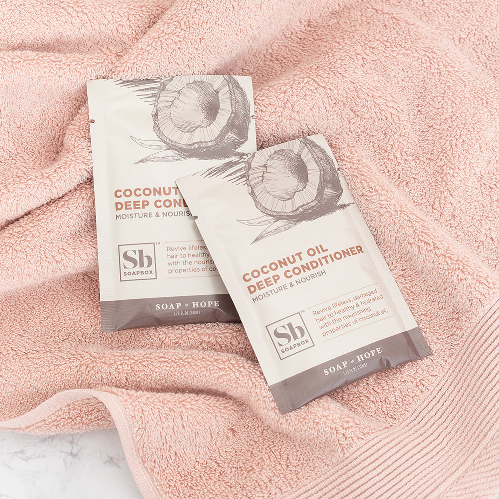 Two white sachets with coconut illustrations and "Coconut Oil Deep Conditioner" text on pink towel.