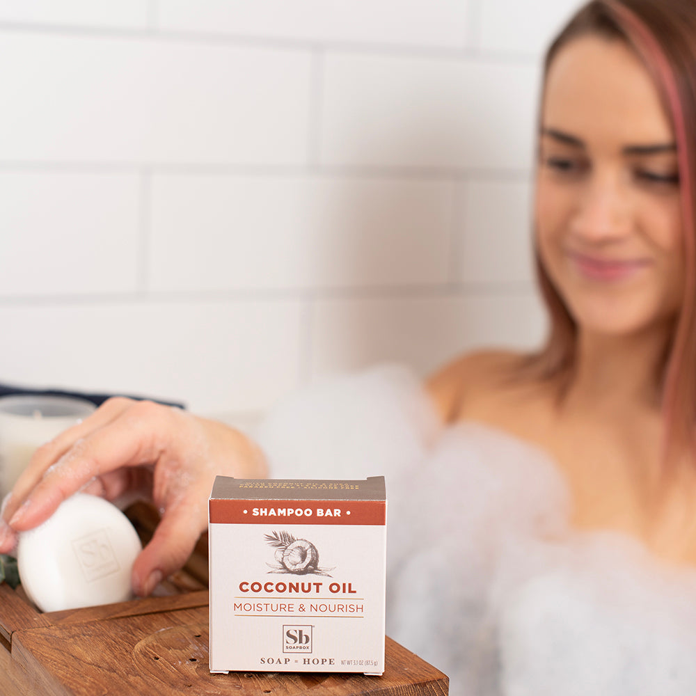 Solid white shampoo bar with red and cream packaging labeled "Coconut Oil Moisture & Nourish" displayed on wooden surface.