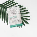 White sachet packet labeled "Tea Tree Soothing Hydration Hair Mask" with turquoise accents, displayed on green palm leaves.