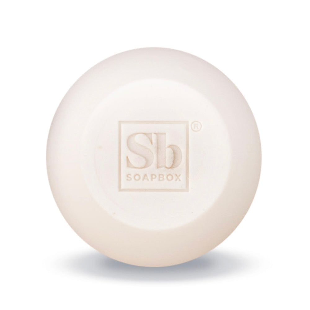 Cream-colored round shampoo bar with embossed "Sb Soapbox" logo on surface.