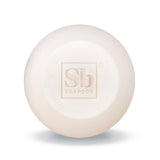 Cream-colored round shampoo bar with embossed "Sb Soapbox" logo on surface.